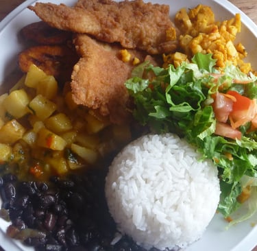 Traditional Casado plate with breaded fish, white rice, black beans, fried plantains, and fresh salad.
