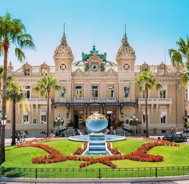 The historic Monte Carlo Casino in Monaco with a fountain and palm trees under a blue sky.