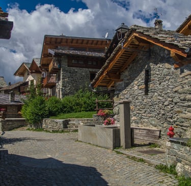 Rustic stone houses and a cobblestone street in a traditional European mountain village.