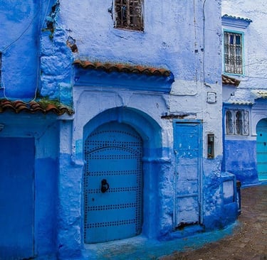 Narrow street in Chefchaouen, Morocco, featuring traditional blue painted walls and arched doors.