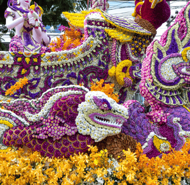 Intricate flower festival float featuring colorful Naga dragon sculptures made of purple and yellow blossoms.