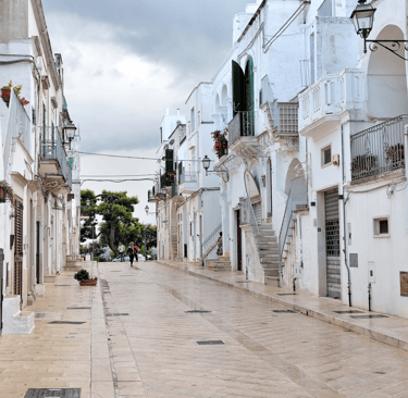 Narrow stone street lined with traditional white houses in a scenic Italian village in Puglia.