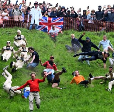 Crowds of people tumbling down a steep green hill during the annual Cooper's Hill Cheese-Rolling competition.