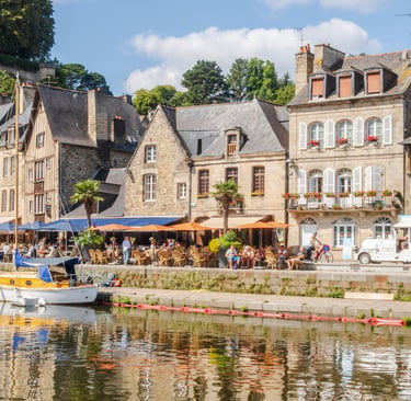 Scenic waterfront with historic stone houses and outdoor cafes in Dinan, Brittany, France.