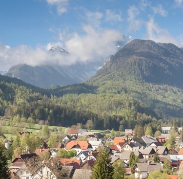 Panoramic view of a scenic mountain village in the Julian Alps with snow-capped peaks and pine forests.