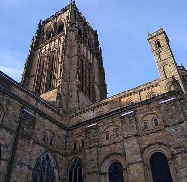 Low-angle view of the historic Durham Cathedral stone towers and gothic architecture against a blue sky.