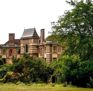 Historic Eltham Palace art deco mansion architecture nestled behind lush green garden trees in London.