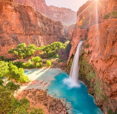Havasu Falls in the Grand Canyon with turquoise water and red rock cliffs at sunrise.