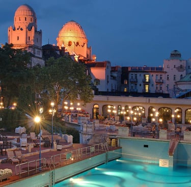 The outdoor thermal pool at Gellert Baths in Budapest illuminated at night with Art Nouveau architecture.