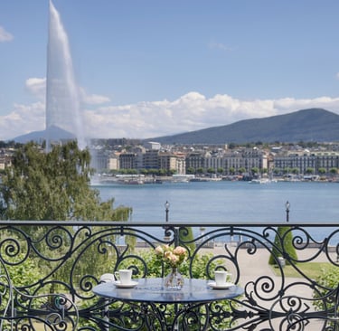 Luxury balcony view of the Jet d'Eau fountain and Lake Geneva with coffee on a bistro table.