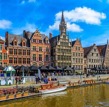 Historic medieval guild houses along the Graslei canal in Ghent, Belgium under a sunny blue sky.