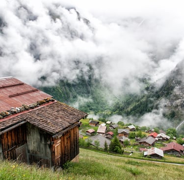 Rustic wooden chalets in a misty Swiss alpine village overlooking a foggy mountain valley.