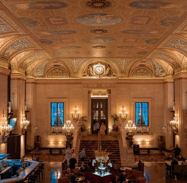 Elegant historic hotel lobby with ornate painted ceilings, gold chandeliers, and a grand marble staircase.