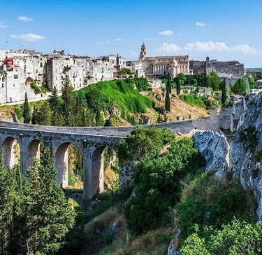 Ancient stone bridge and historic white buildings in the scenic ravine town of Gravina in Puglia, Italy.