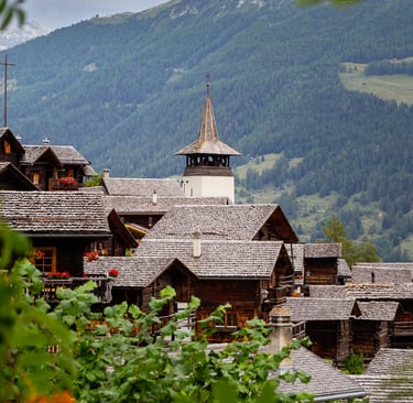 Rustic wooden chalets and a church steeple in a traditional Swiss mountain village.