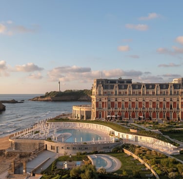 Luxury Hôtel du Palais in Biarritz at sunset with a view of the pool, beach, and Phare de Biarritz lighthouse.