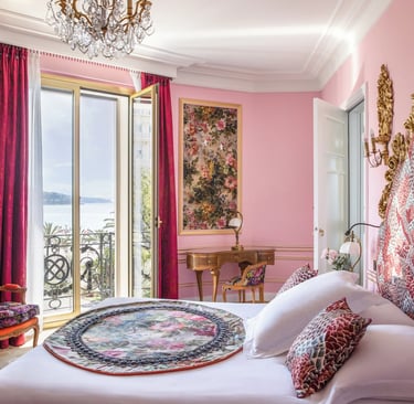 Luxury pink hotel room with crystal chandelier, ornate gold headboard, and balcony overlooking the sea.
