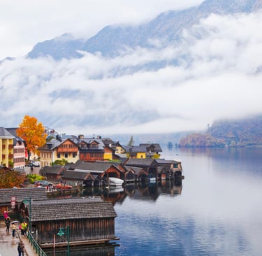 Scenic lakeside village of Hallstatt, Austria, with mist-covered mountains and traditional wooden boathouses.