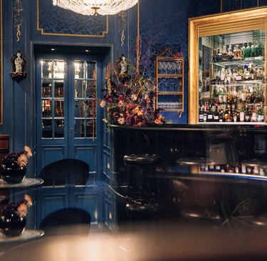 Elegant luxury bar interior featuring blue damask wallpaper, a gold liquor cabinet, and a crystal chandelier.