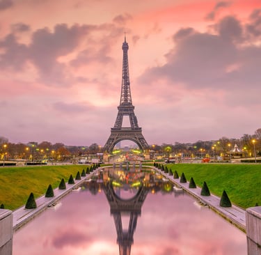 The Eiffel Tower at sunset with pink clouds reflected in the Trocadero Gardens fountain in Paris.