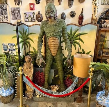A life-sized Creature from the Black Lagoon statue displayed in a tropical tiki-themed room with masks.
