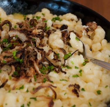 Traditional German Käsespätzle topped with crispy fried onions and fresh chives in a black pan.