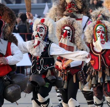 Performers in traditional Bulgarian Kukeri costumes and masks dancing with large bells during a festival.