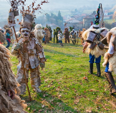 Participants in traditional European pagan carnival costumes with burlap, cowbells, and birch bark masks in a field.