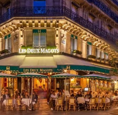 The illuminated exterior of Les Deux Magots cafe in Paris with outdoor terrace seating at night.