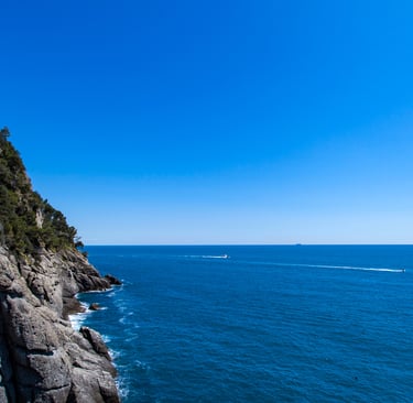 Panoramic view of steep rocky cliffs and the deep blue Mediterranean Sea under a clear sky in Portofino, Italy.