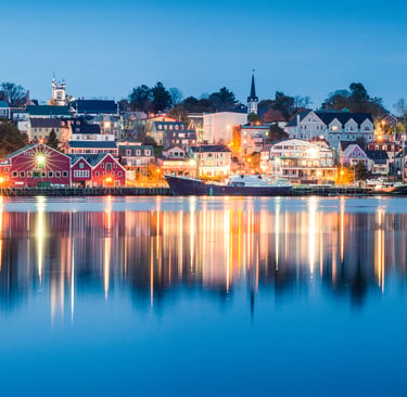 A panoramic night view of Lunenburg harbor with colorful buildings reflecting in the calm water.