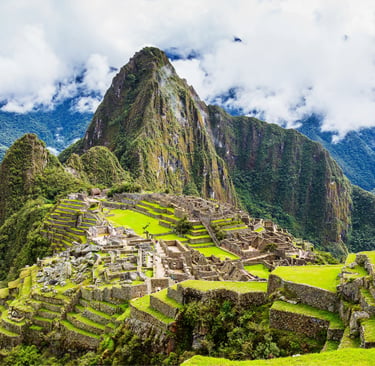 Ancient Inca ruins of Machu Picchu nestled in the green Peruvian Andes mountains under a cloudy sky.
