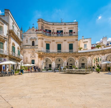 Sunny view of Piazza Maria Immacolata in Martina Franca, Italy, featuring historic Baroque architecture and cafes.