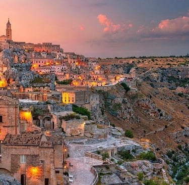 A panoramic view of Matera's ancient Sassi district at sunset with glowing lights and stone architecture.