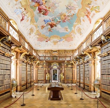 Ornate Baroque library with wooden bookshelves and a colorful fresco painted on the ceiling.