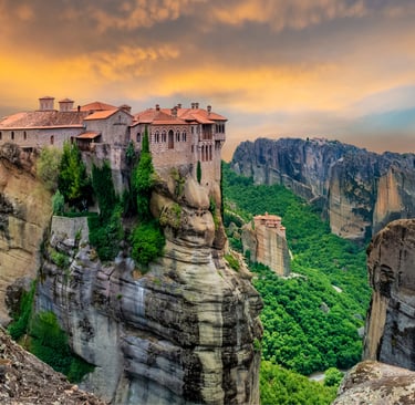Ancient Meteora monasteries perched on steep rock cliffs in Greece during a vibrant sunset.