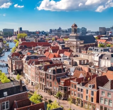 Aerial view of Leiden city center featuring traditional Dutch architecture, canals, and historic churches under a blue sky.