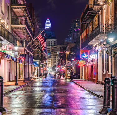 Neon lights reflect on the wet pavement of Bourbon Street in the New Orleans French Quarter at night.