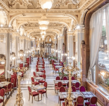 Elegant New York Cafe interior in Budapest with ornate gold ceilings, marble columns, and red velvet chairs.