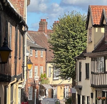 Traditional half-timbered buildings and brick houses lining a narrow historic street in a charming English village.