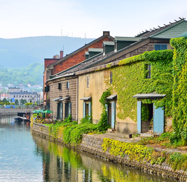 Historic ivy-covered stone warehouses along the scenic Otaru Canal in Hokkaido, Japan.