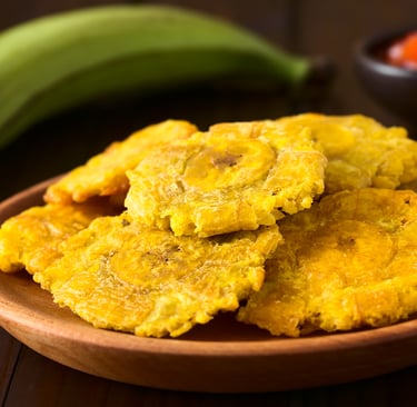 Crispy fried green plantains or tostones served on a wooden plate with a side of salsa.