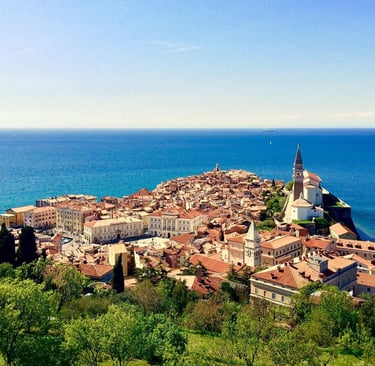 Elevated view of Piran, Slovenia, a historic coastal town with terracotta rooftops, a bell tower, and lush green trees