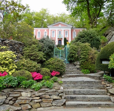 Stone steps leading to a pink Georgian house in Portmeirion Village surrounded by lush green gardens.