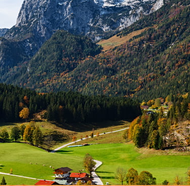 Scenic landscape of an Alpine village in autumn with traditional houses, green meadows, and rugged mountains.