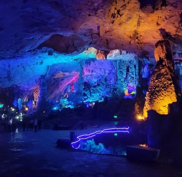 A limestone cave with colorful LED lighting illuminating stalactites and stalagmites.