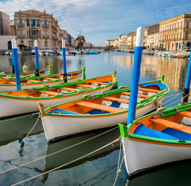 Colorful traditional fishing boats moored in a canal in Sète, France, lined with historic buildings.