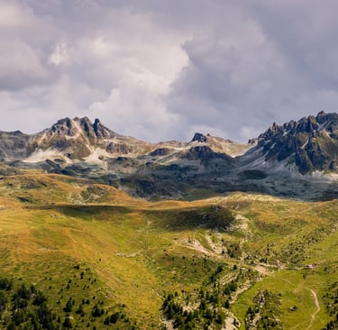 Panoramic view of jagged alpine mountain peaks and green valley slopes under a cloudy sky.