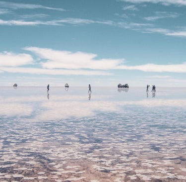 Tourists walking on the reflective Salar de Uyuni salt flats under a blue sky in Bolivia.