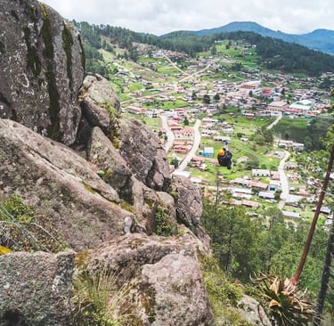 A person zip lining over a scenic mountain town surrounded by lush green pine forests.